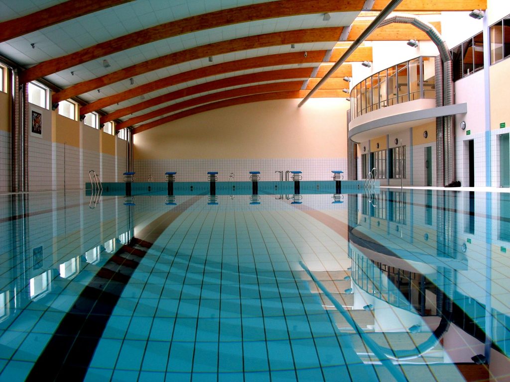 Spacious indoor swimming pool with wooden beams and tiled floor.