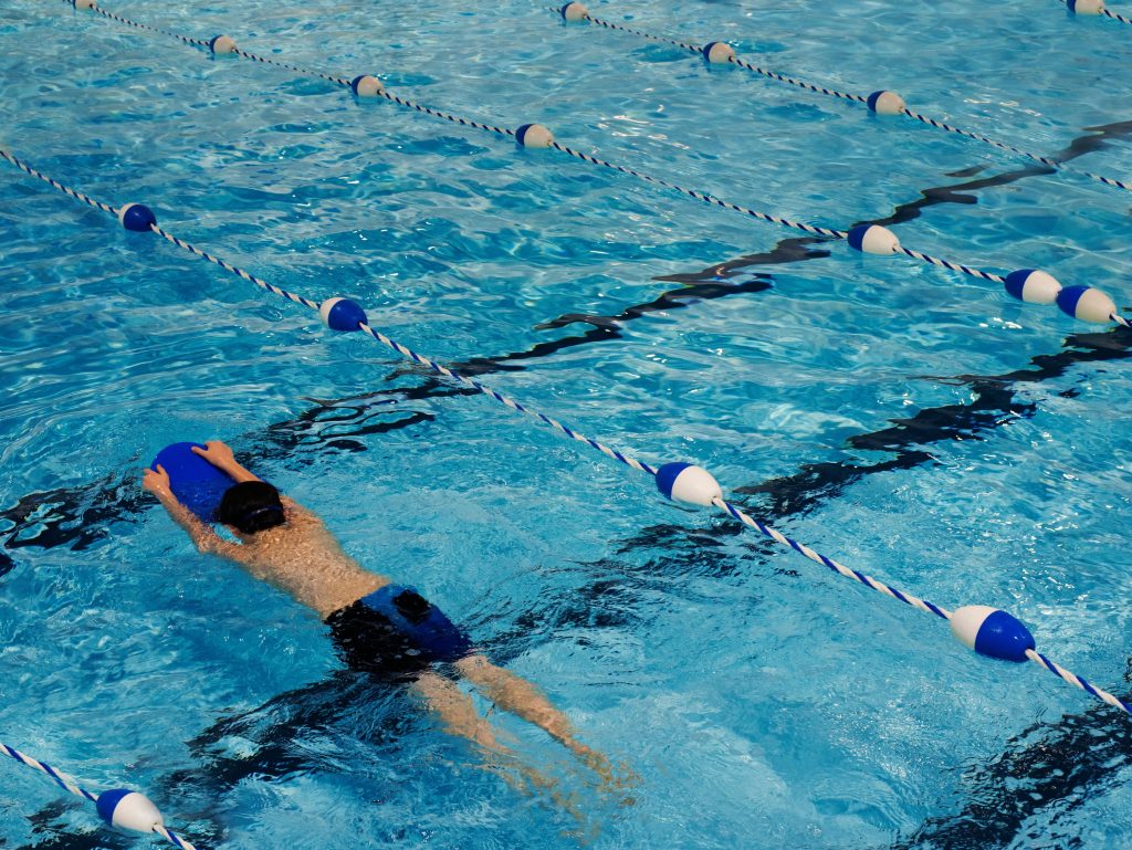 A young swimmer practicing with a kickboard in a swimming pool on a sunny day.