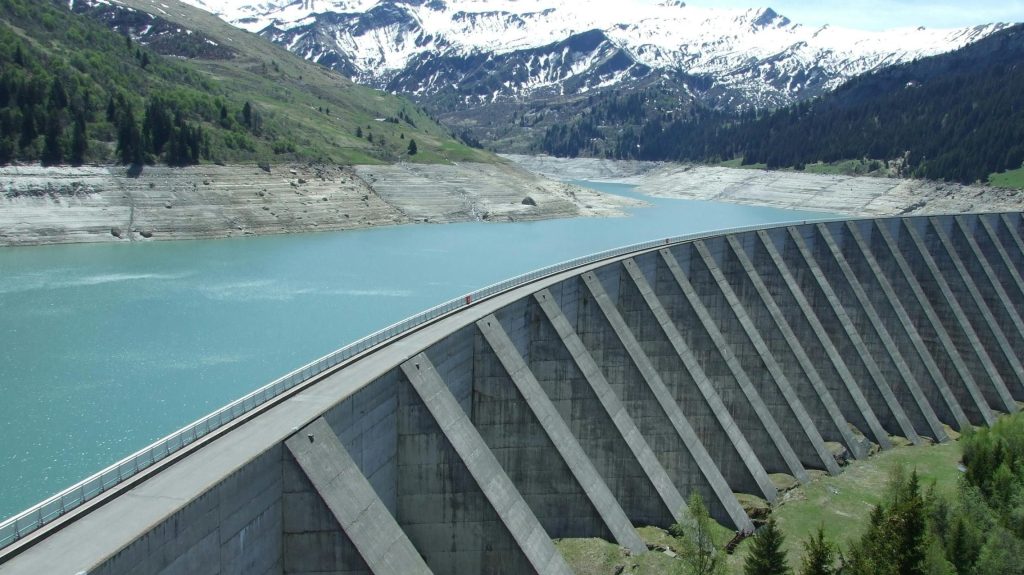 A breathtaking view of a dam amidst a serene alpine landscape with snow-capped mountains.