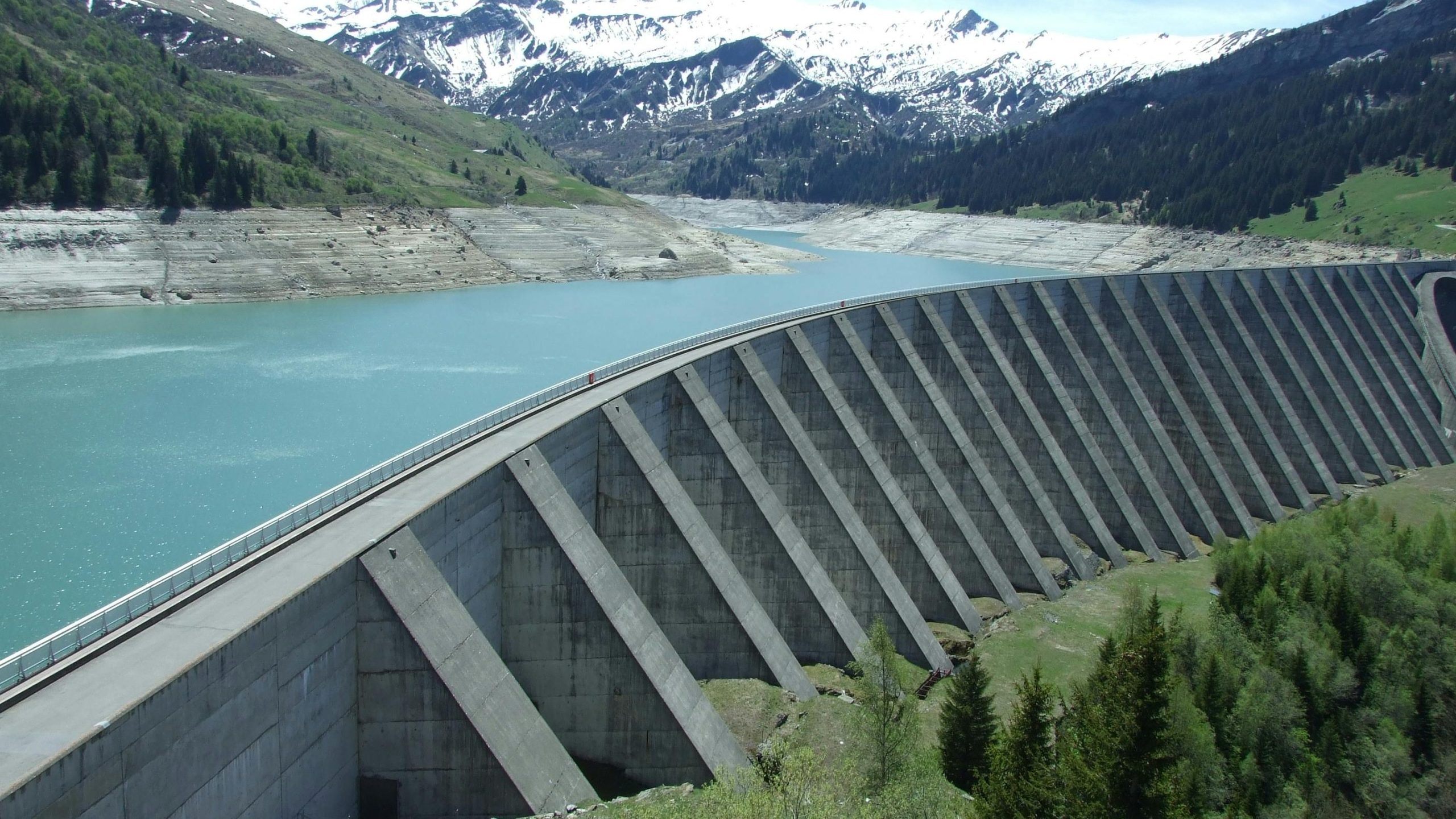 A breathtaking view of a dam amidst a serene alpine landscape with snow-capped mountains.